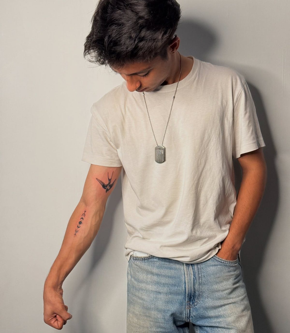 Young man showing a small black bird tattoo on his inner bicep.