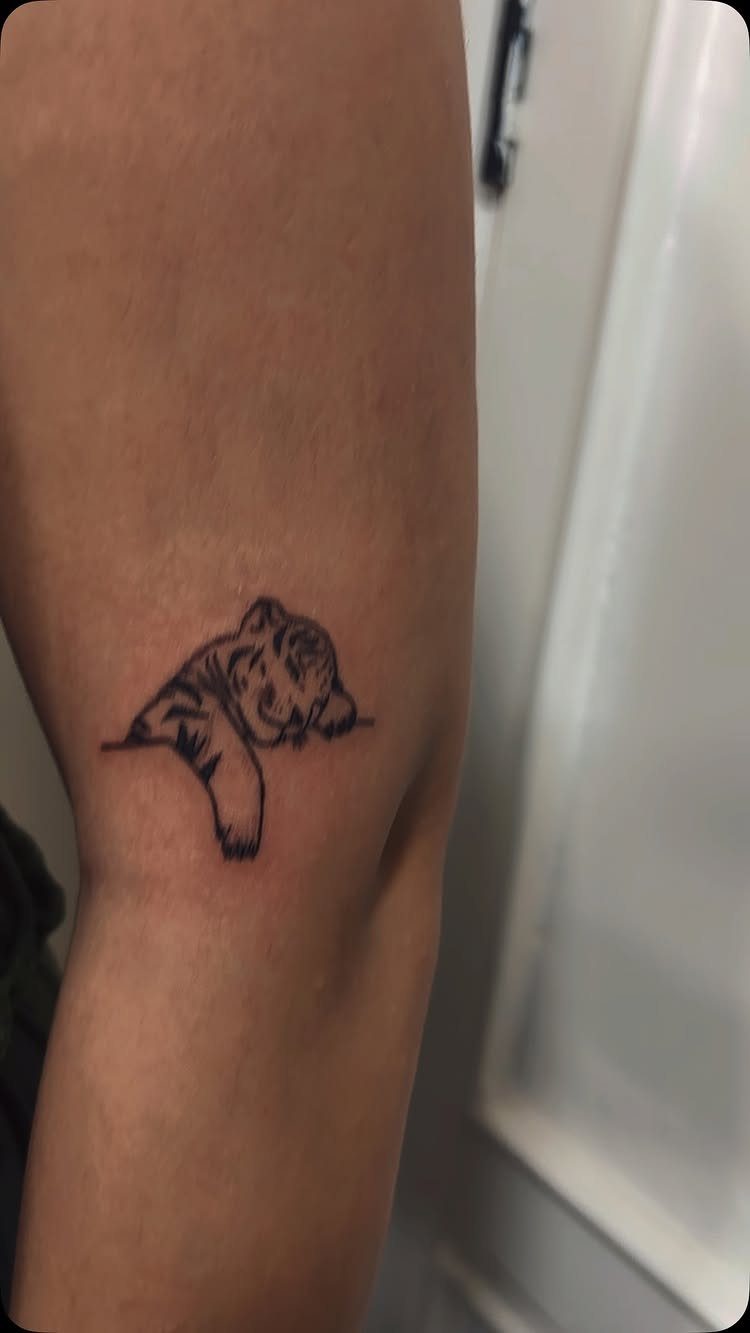 Small black ink bear tattoo peeking on the inner bicep of an arm