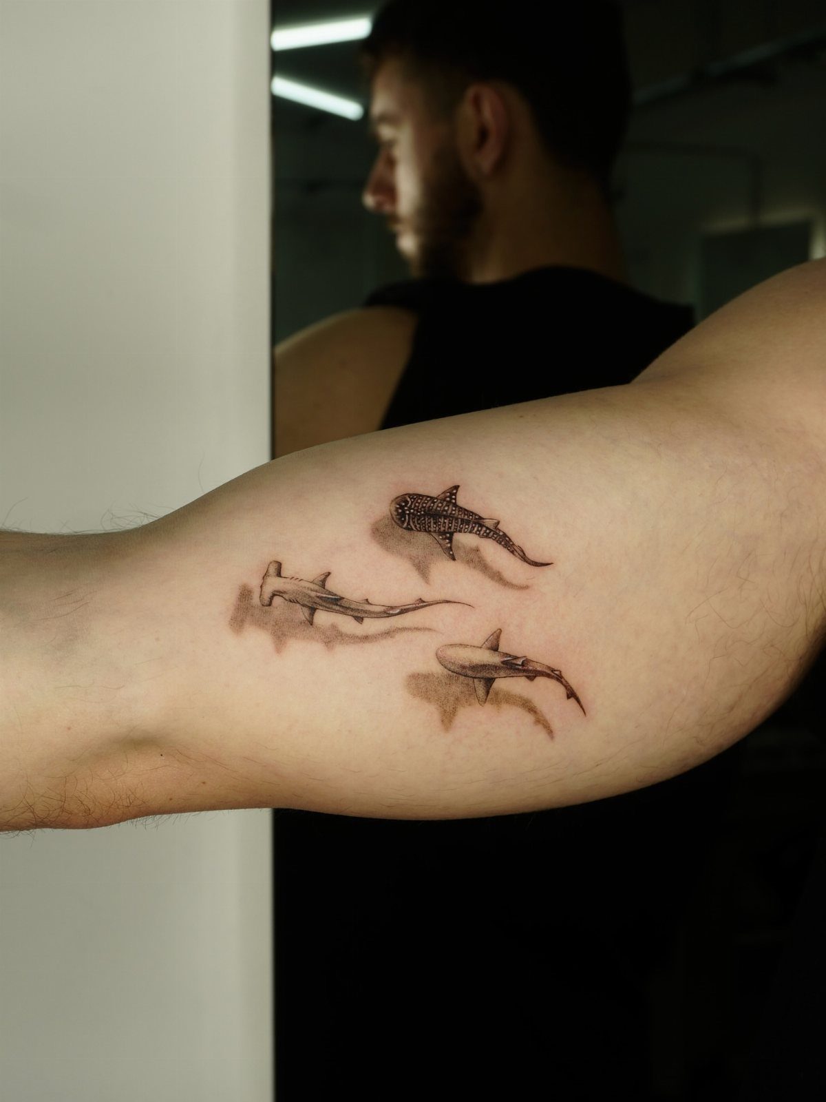 Three small shark tattoos on the inner bicep of a person's arm.