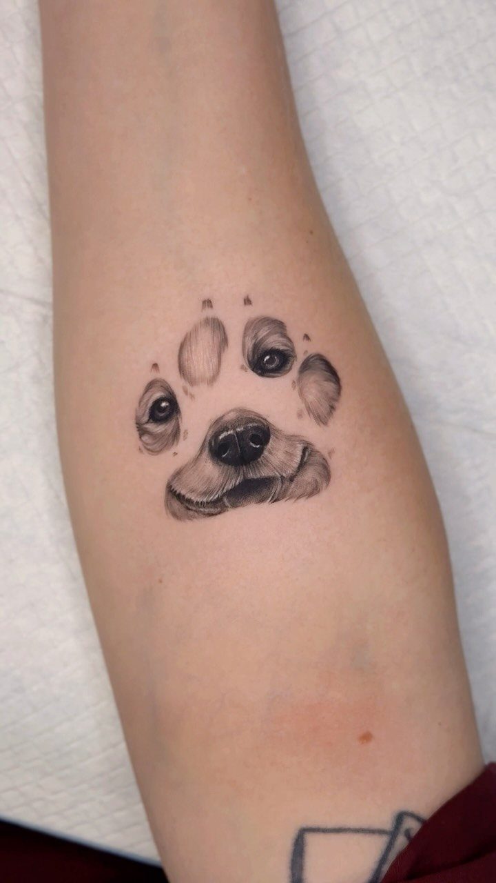 Dog face tattoo integrated into a paw print on a person's arm