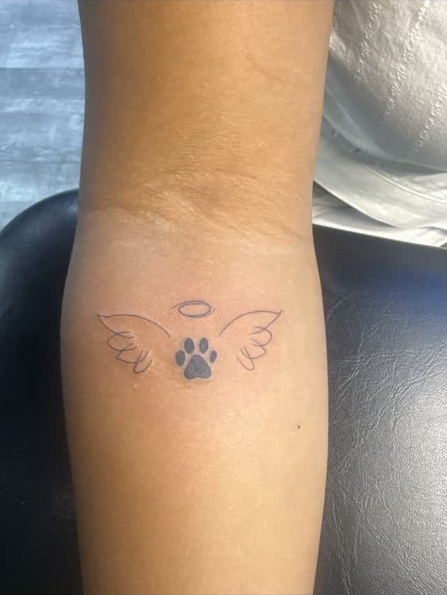 Dog paw print tattoo with wings and a halo on a forearm