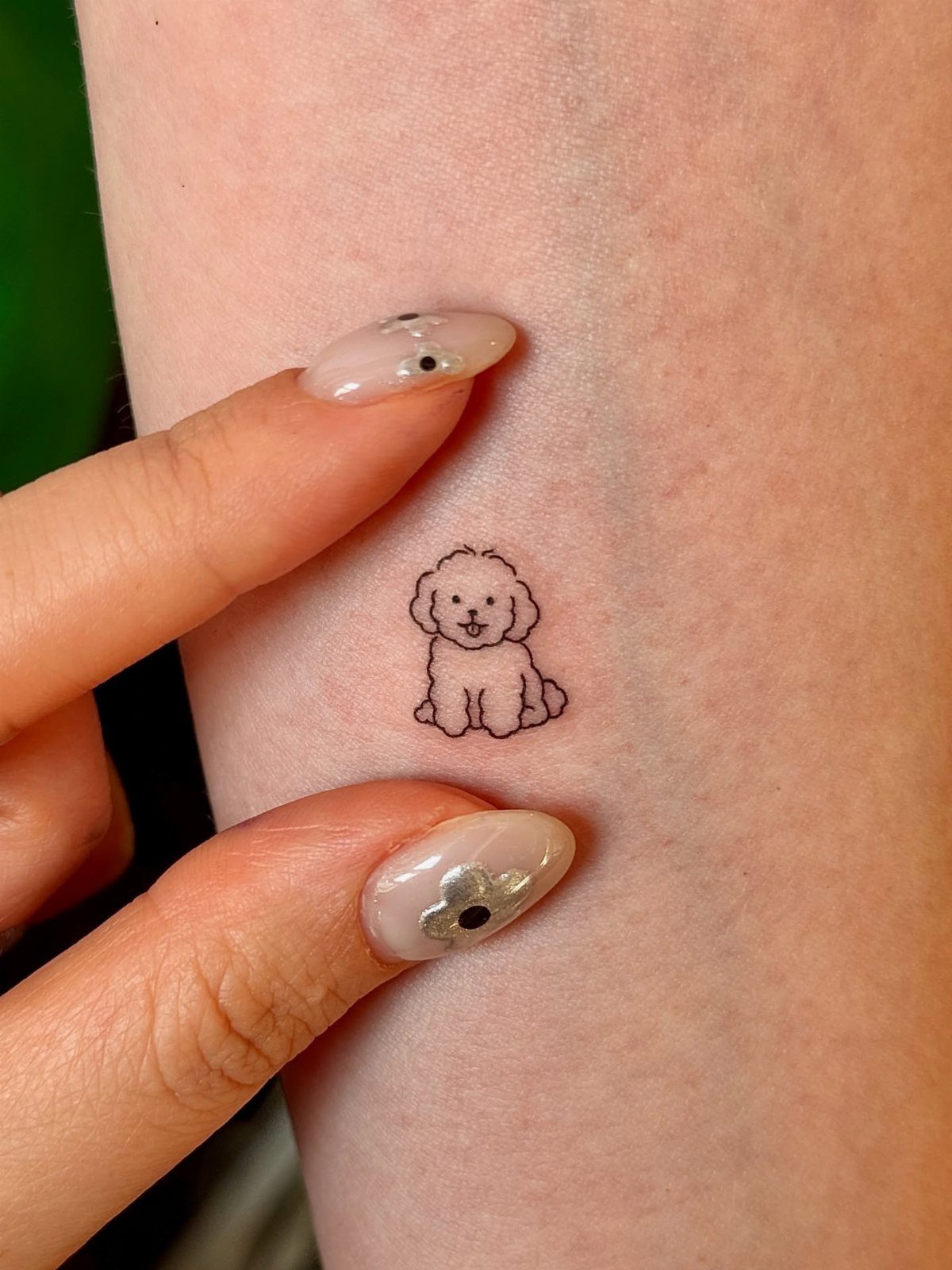 Small black line-art tattoo of a fluffy dog on a person's skin.