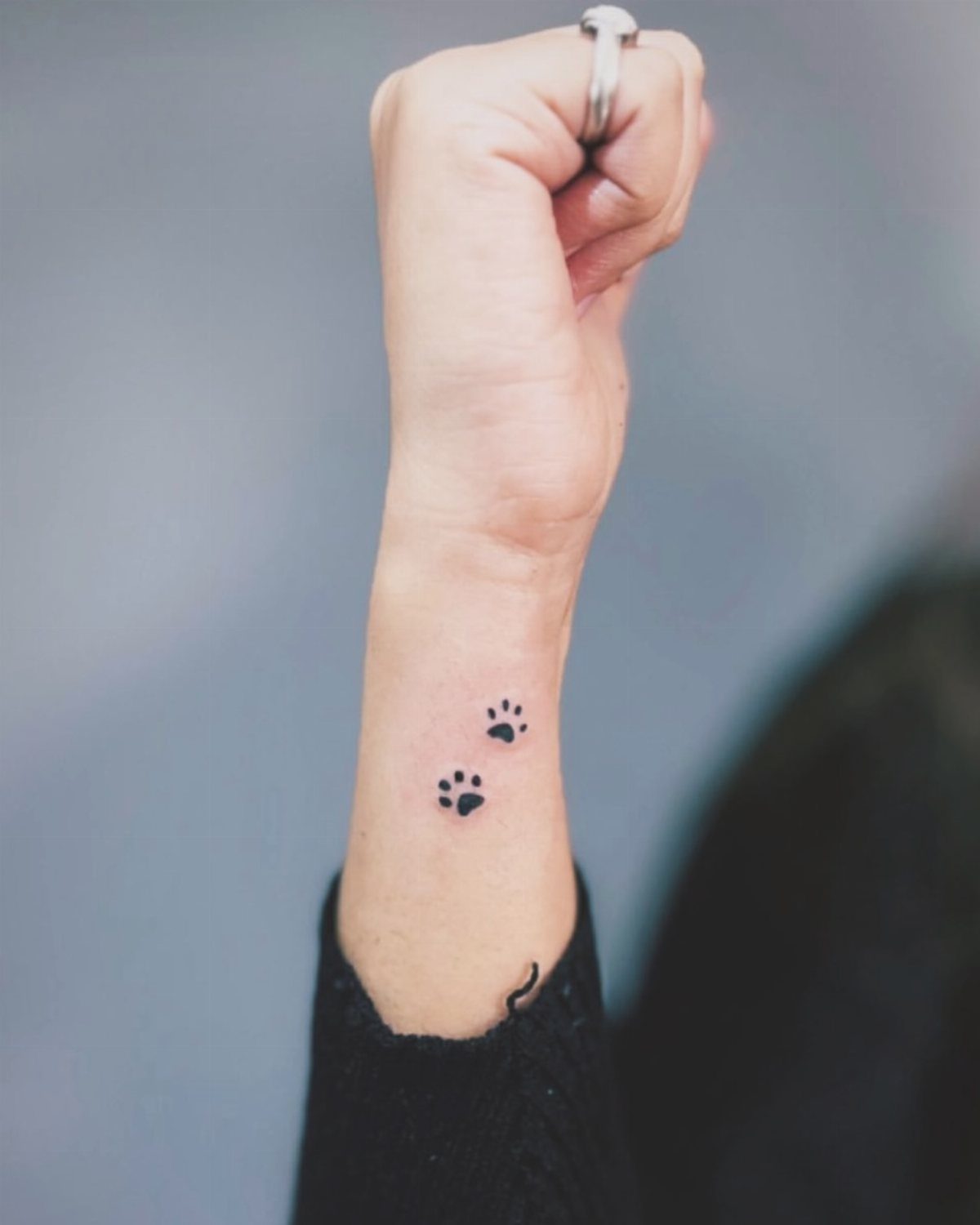 Two small black pawprint tattoos on a person's inner wrist