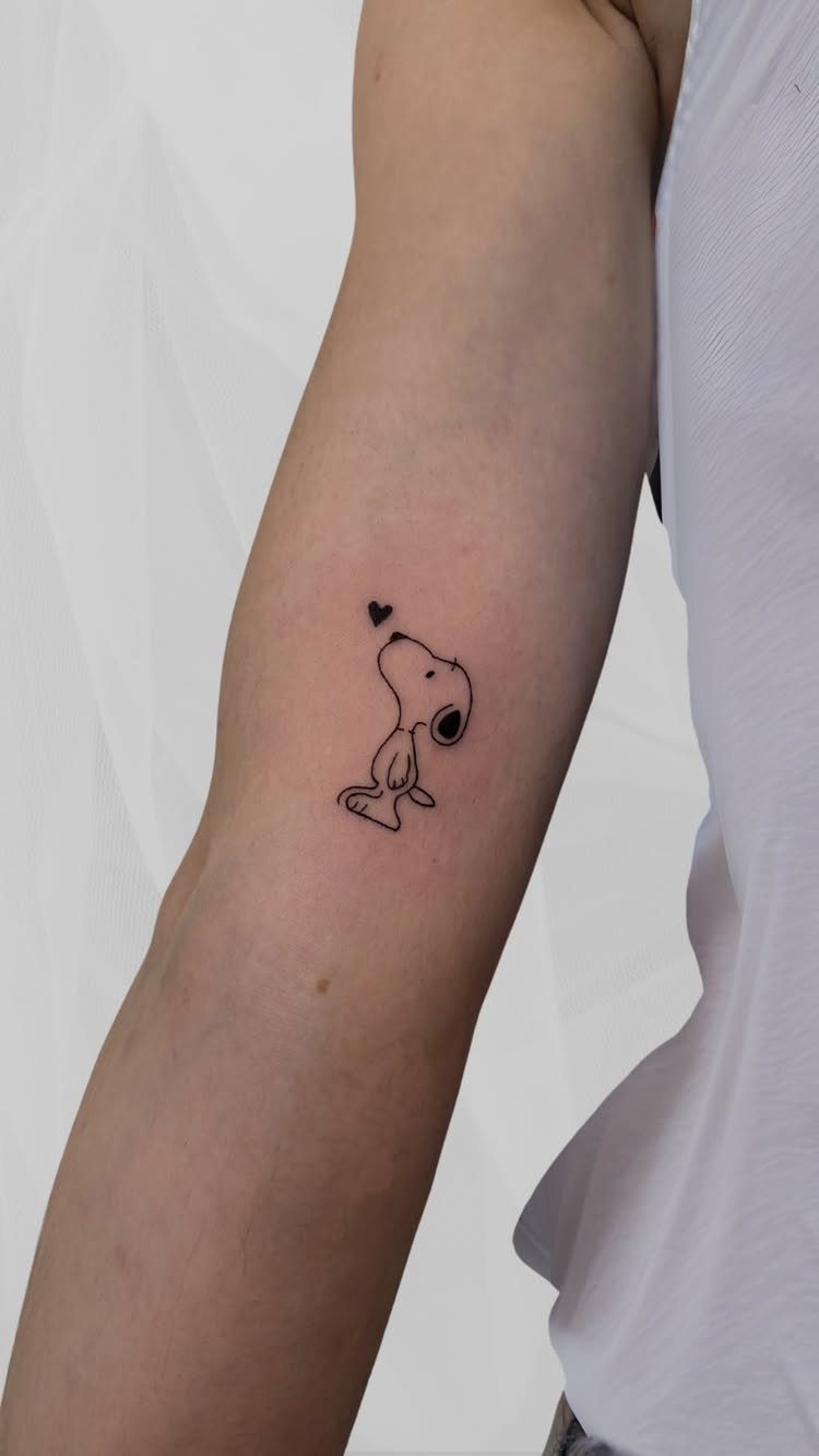 Snoopy dog tattoo with a small heart on a person's inner forearm
