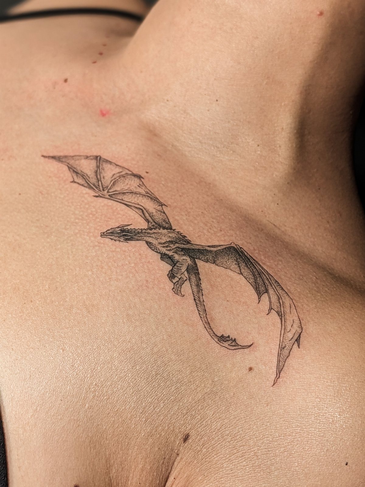 Small black and grey dragon tattoo on a person's upper chest area.