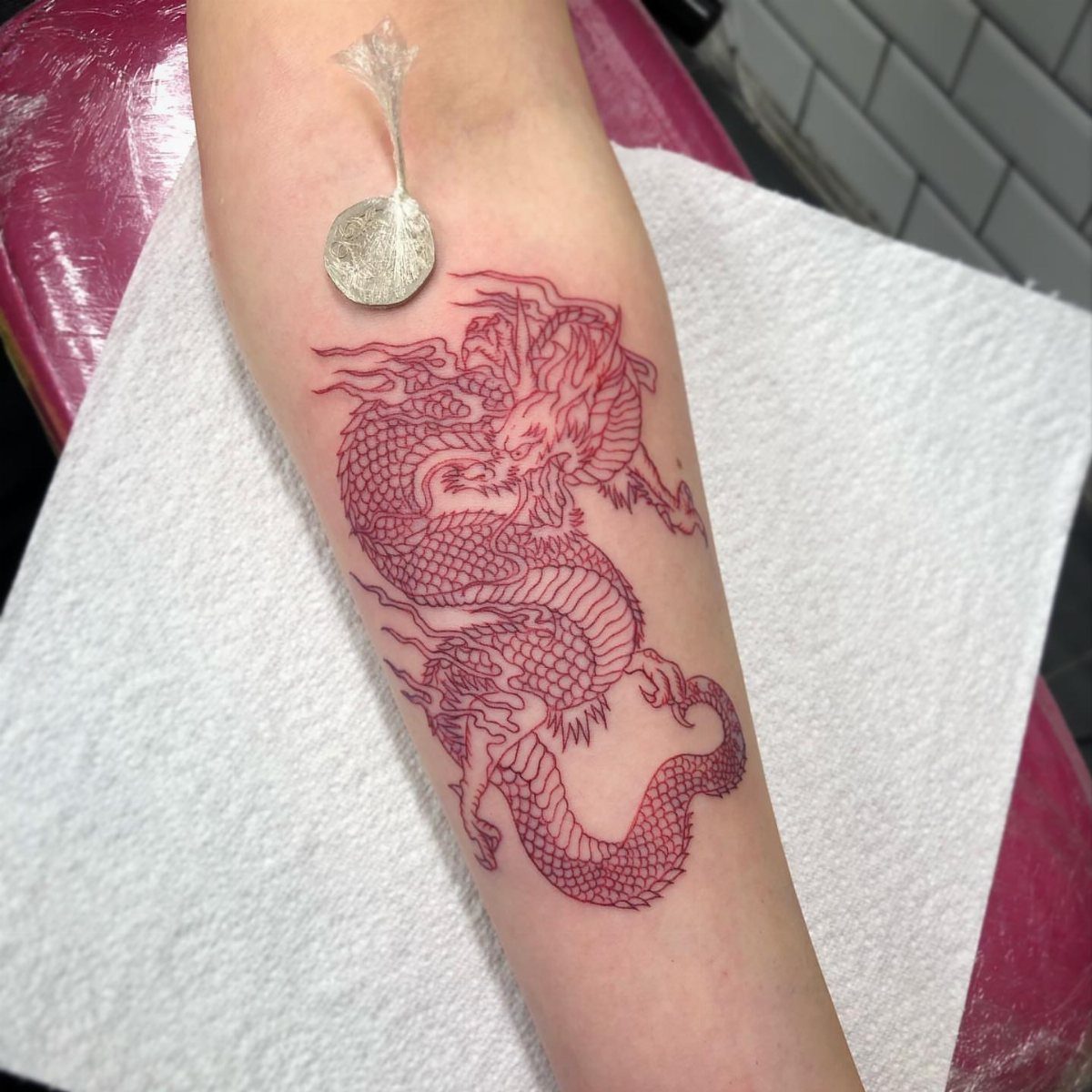 Red dragon tattoo on a forearm with a silver coin for scale
