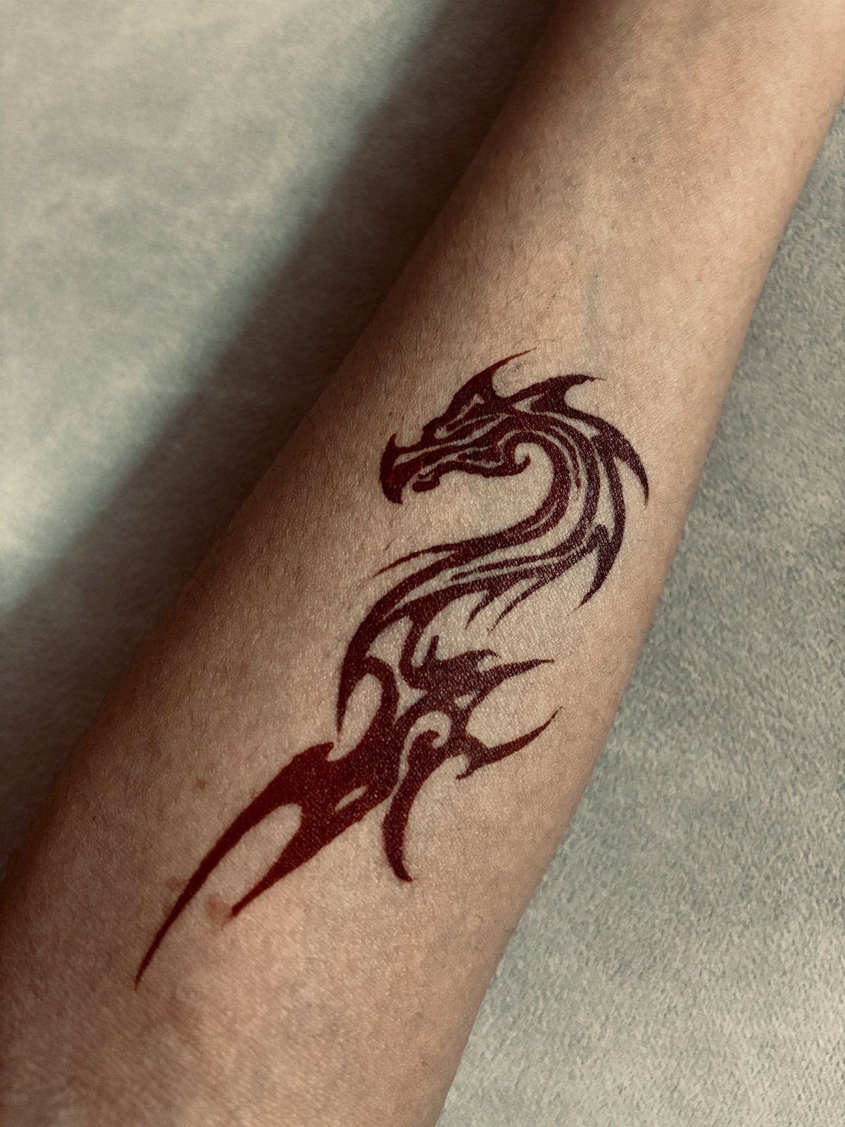 Small dark red tribal dragon tattoo with sharp lines on a forearm