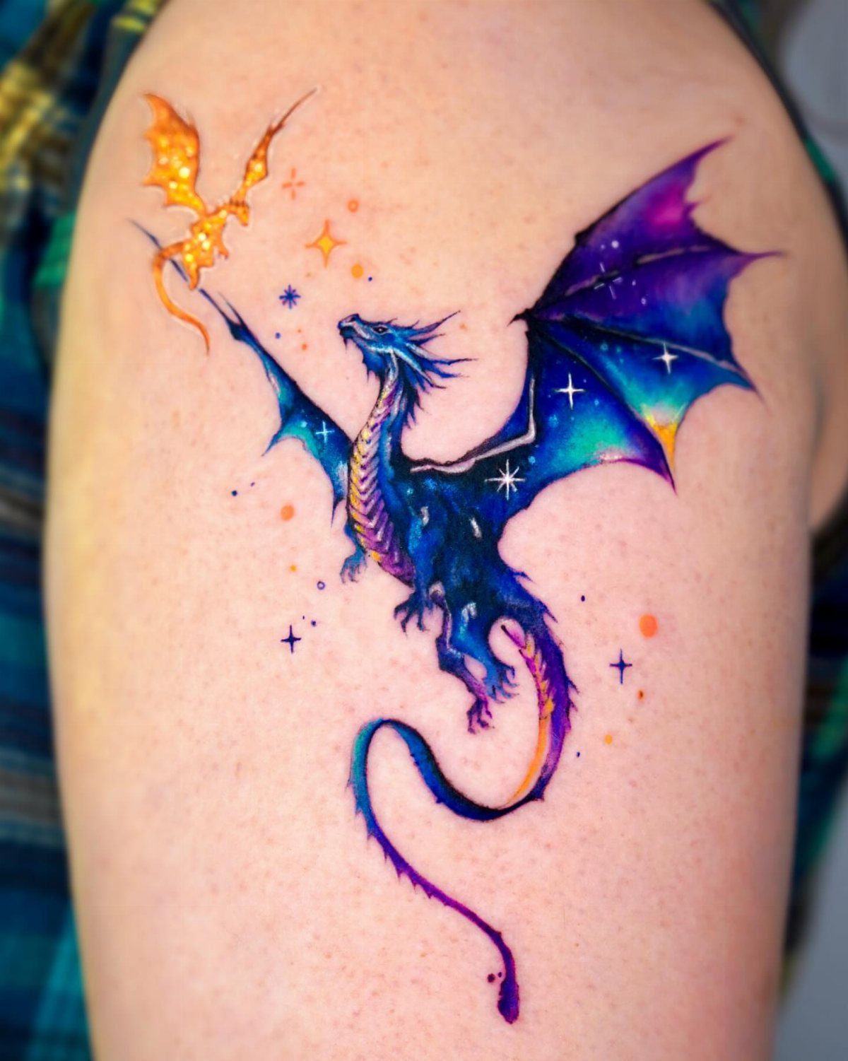 Vibrant watercolor tattoo of a blue and purple dragon on a person's arm.