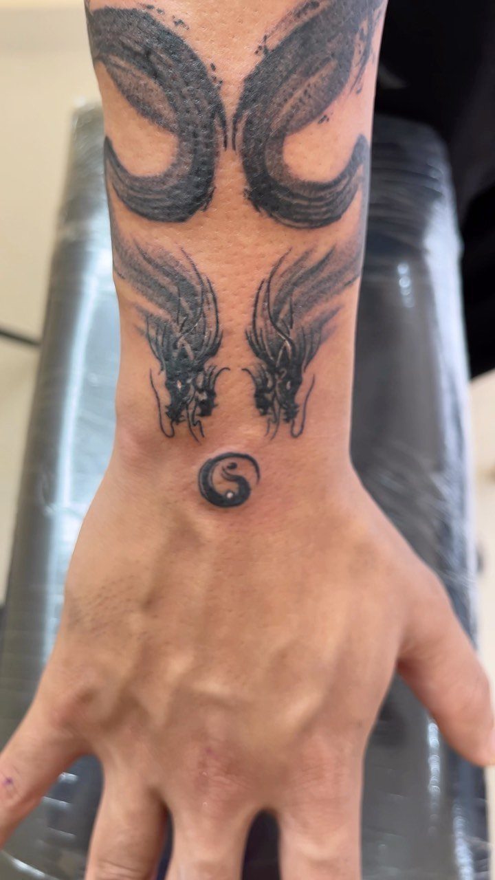 Two dragon head tattoos facing each other above a small yin-yang symbol on a wrist.