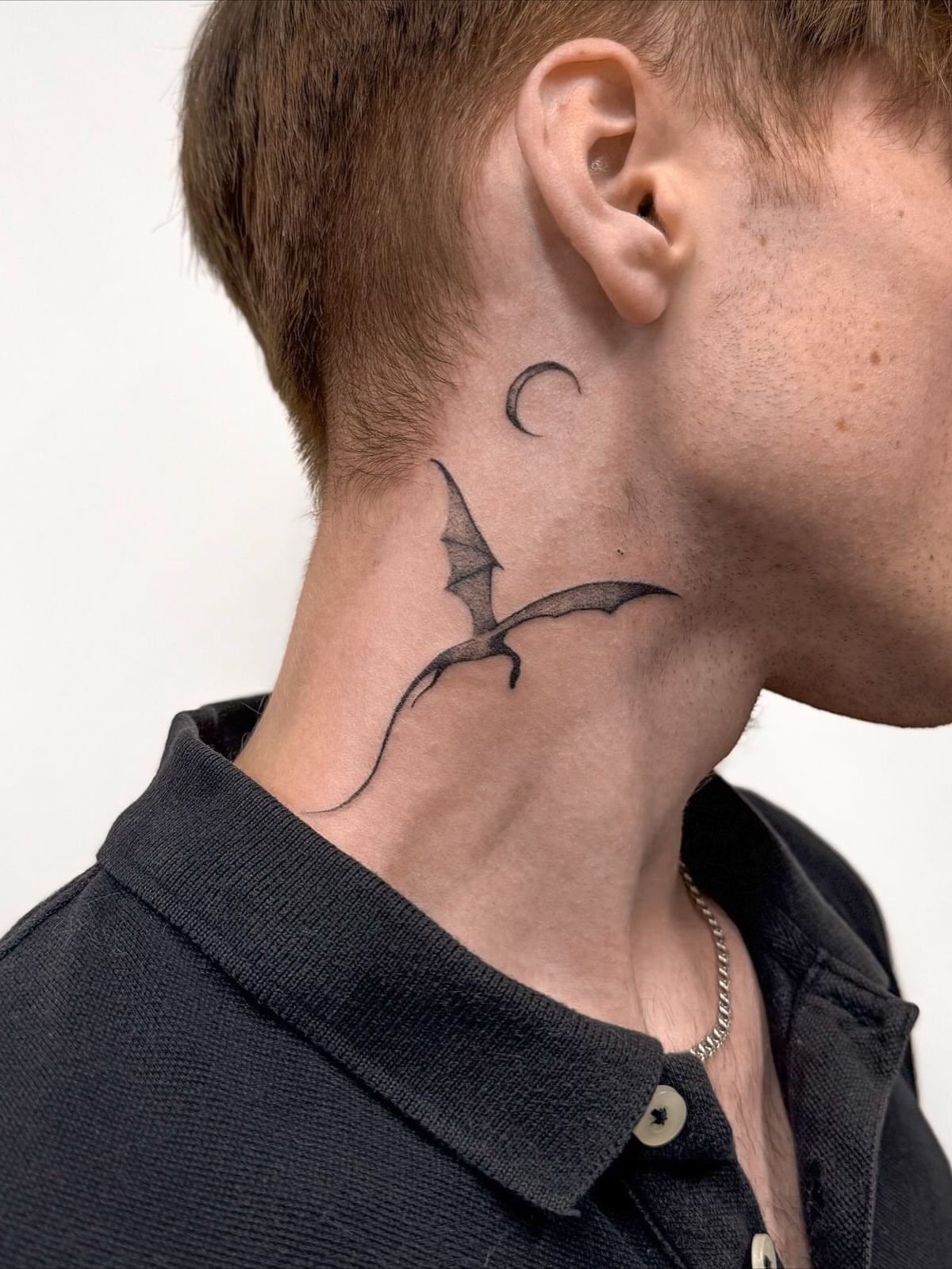 Bat and crescent moon tattoos on the side of a person's neck.