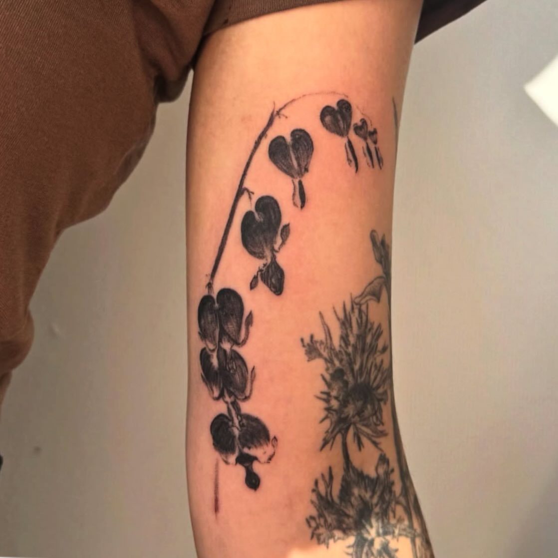 Black ink tattoo of heart-shaped flowers on a person's lower leg.