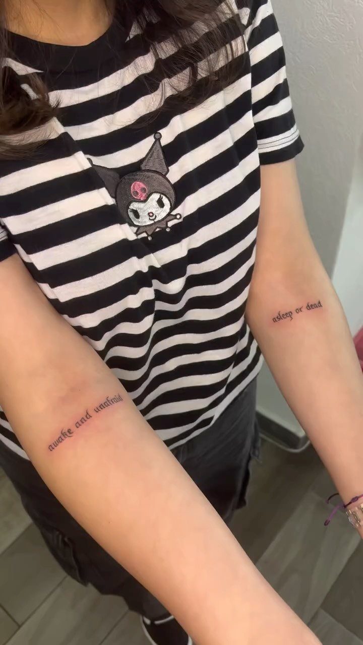 Red text tattoos on inner forearms of a person in a striped shirt.