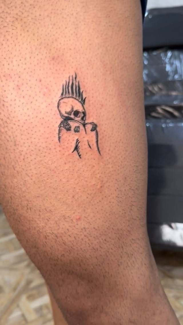 Small black ink tattoo of a curled-up figure with spiky hair on a leg.