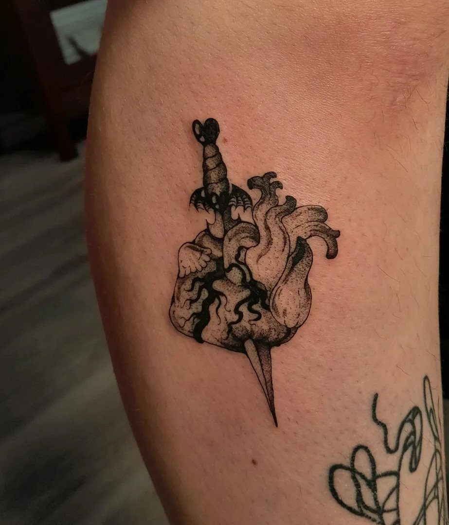 Anatomical heart pierced by a dagger tattoo in black ink on skin.