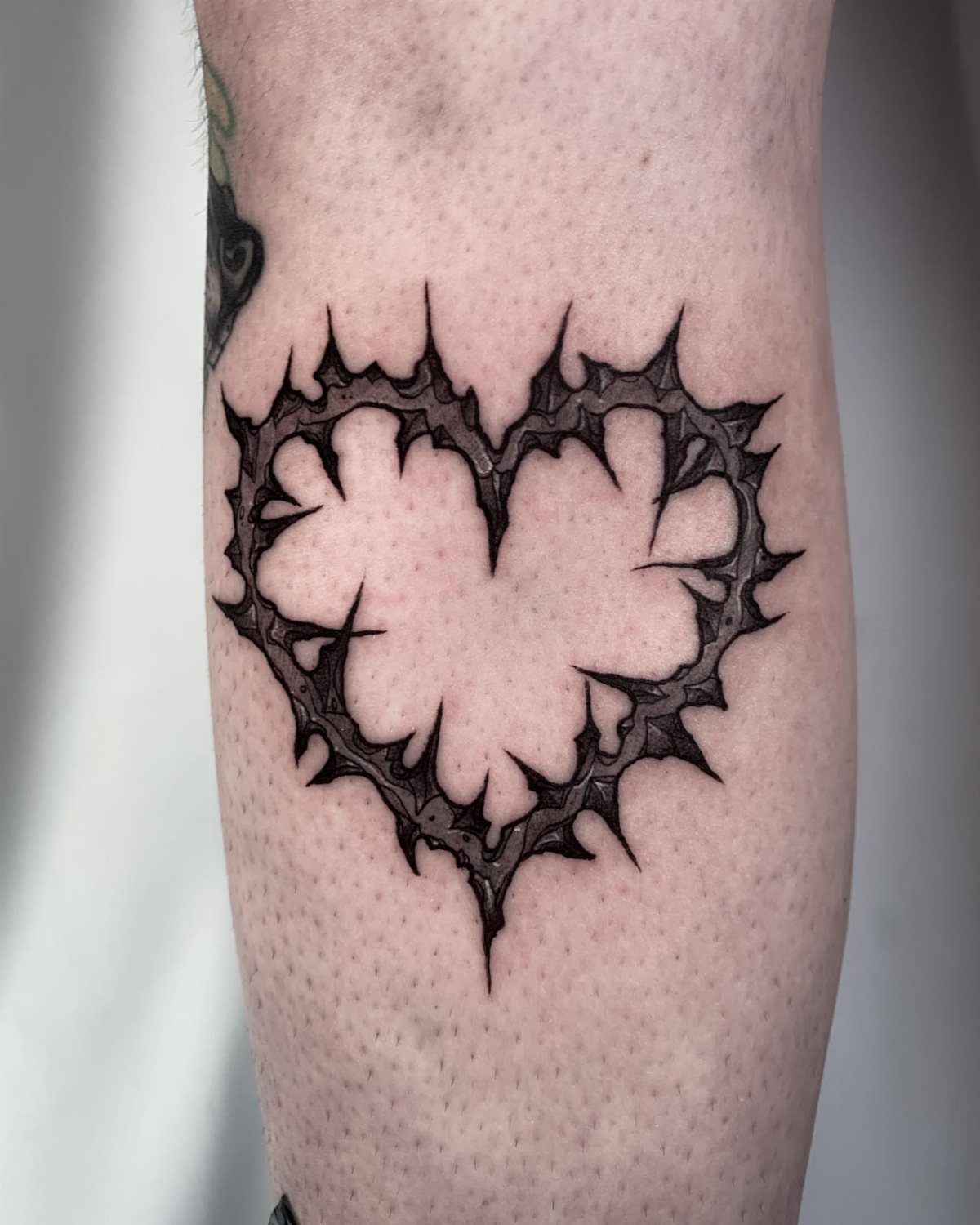Heart-shaped thorn tattoo in black ink on a person's skin.
