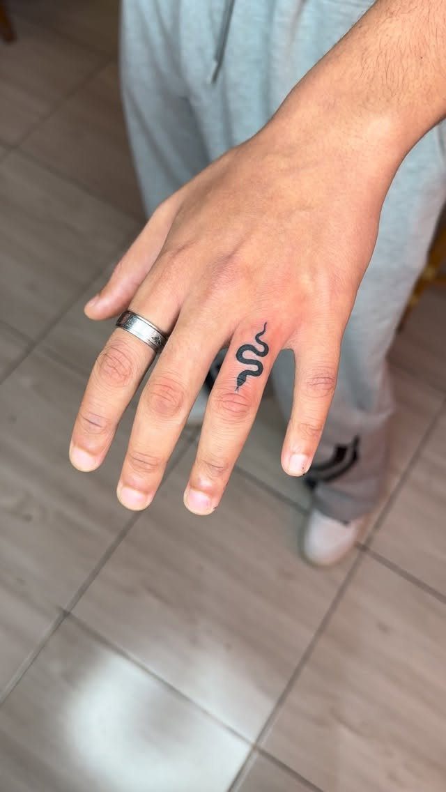 Small black snake tattoo on the ring finger of a person's hand