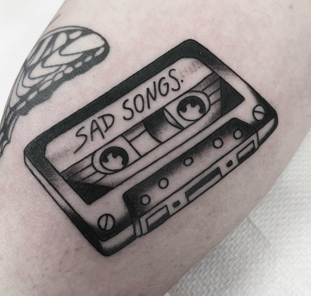 Cassette tape tattoo with the words SAD SONGS written on the label.