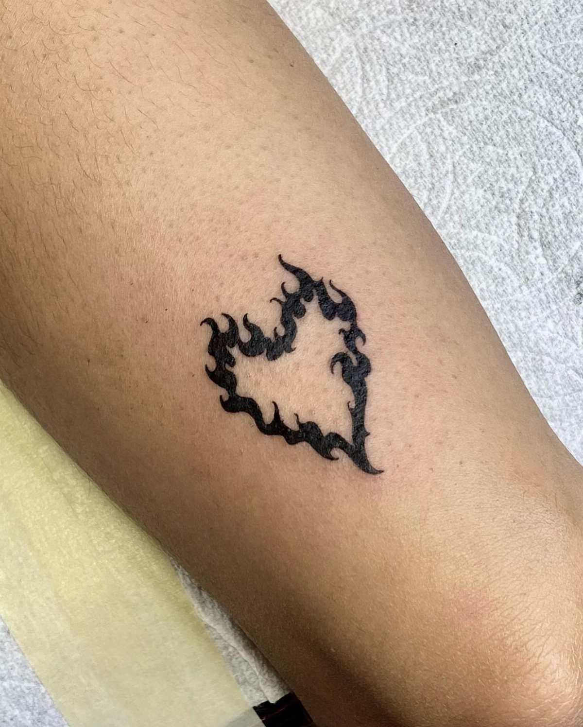Flame heart tattoo in black ink on a person's arm.
