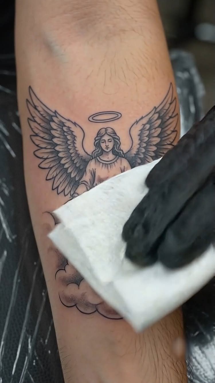 Guardian angel tattoo with wings and halo on a forearm being wiped clean.