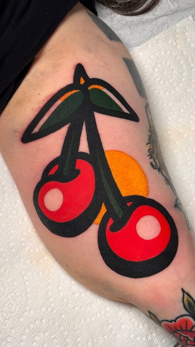 Cherry tattoo with red fruit and green leaves on a person's arm.