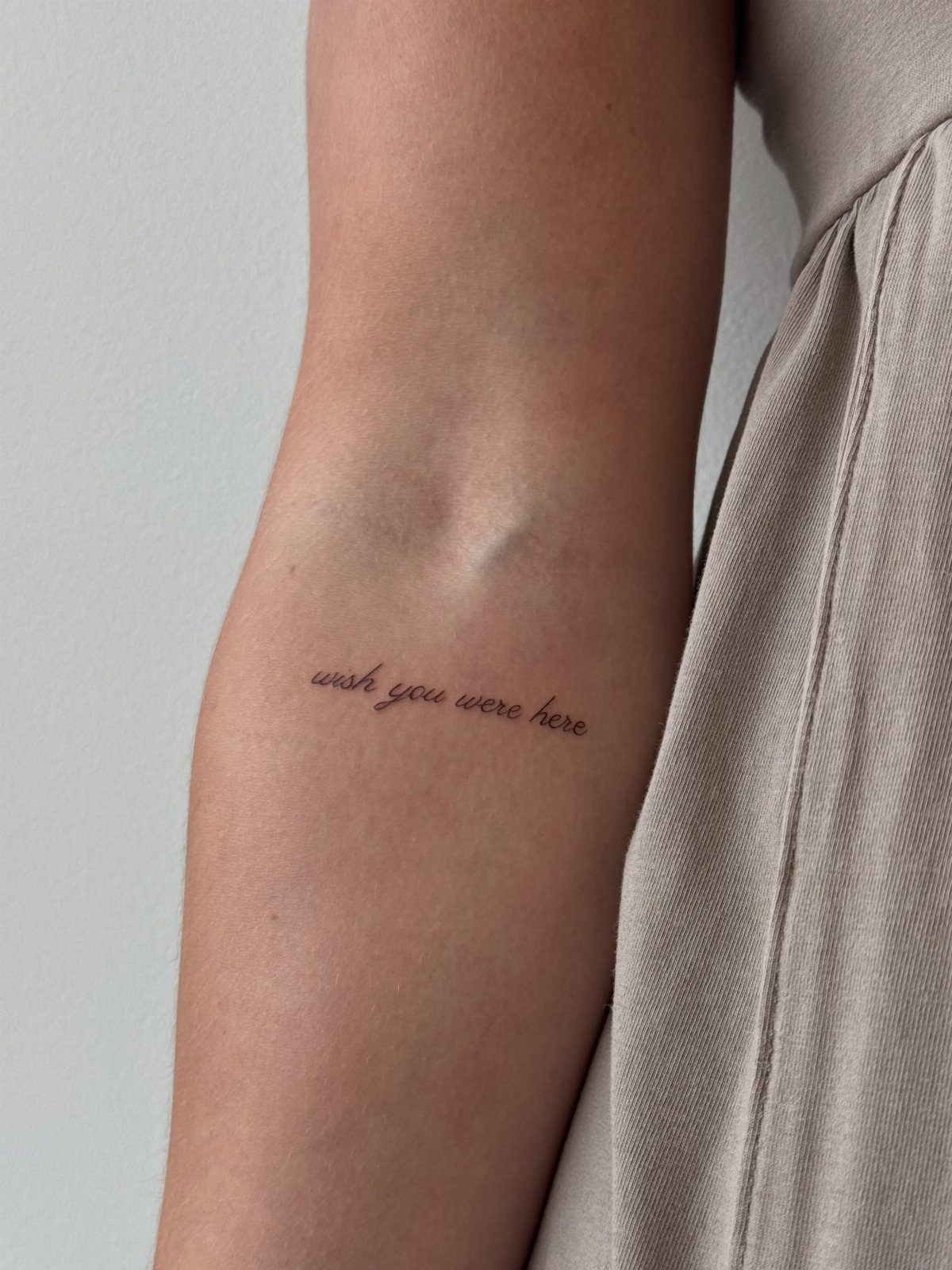 Small script tattoo on a forearm reading wish you were here in black ink