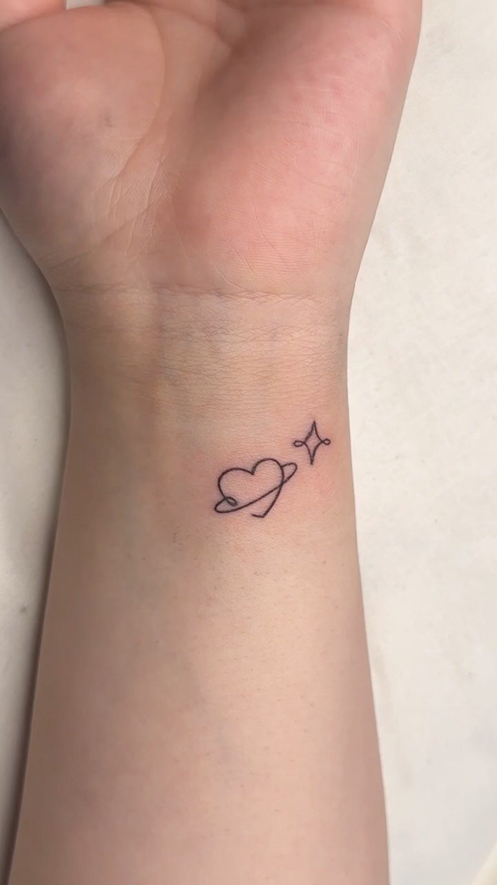 Small heart tattoo with a planetary ring and star on a wrist