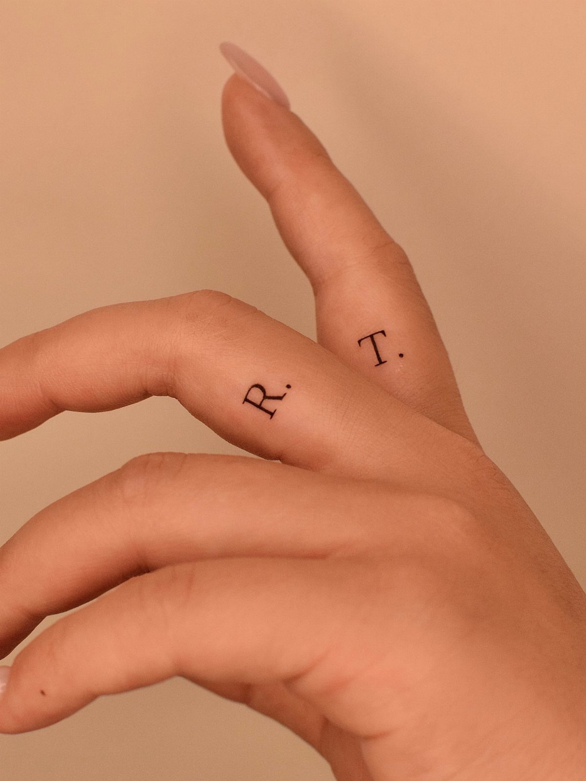 Small black letter tattoos on the inner fingers of a person's hand.