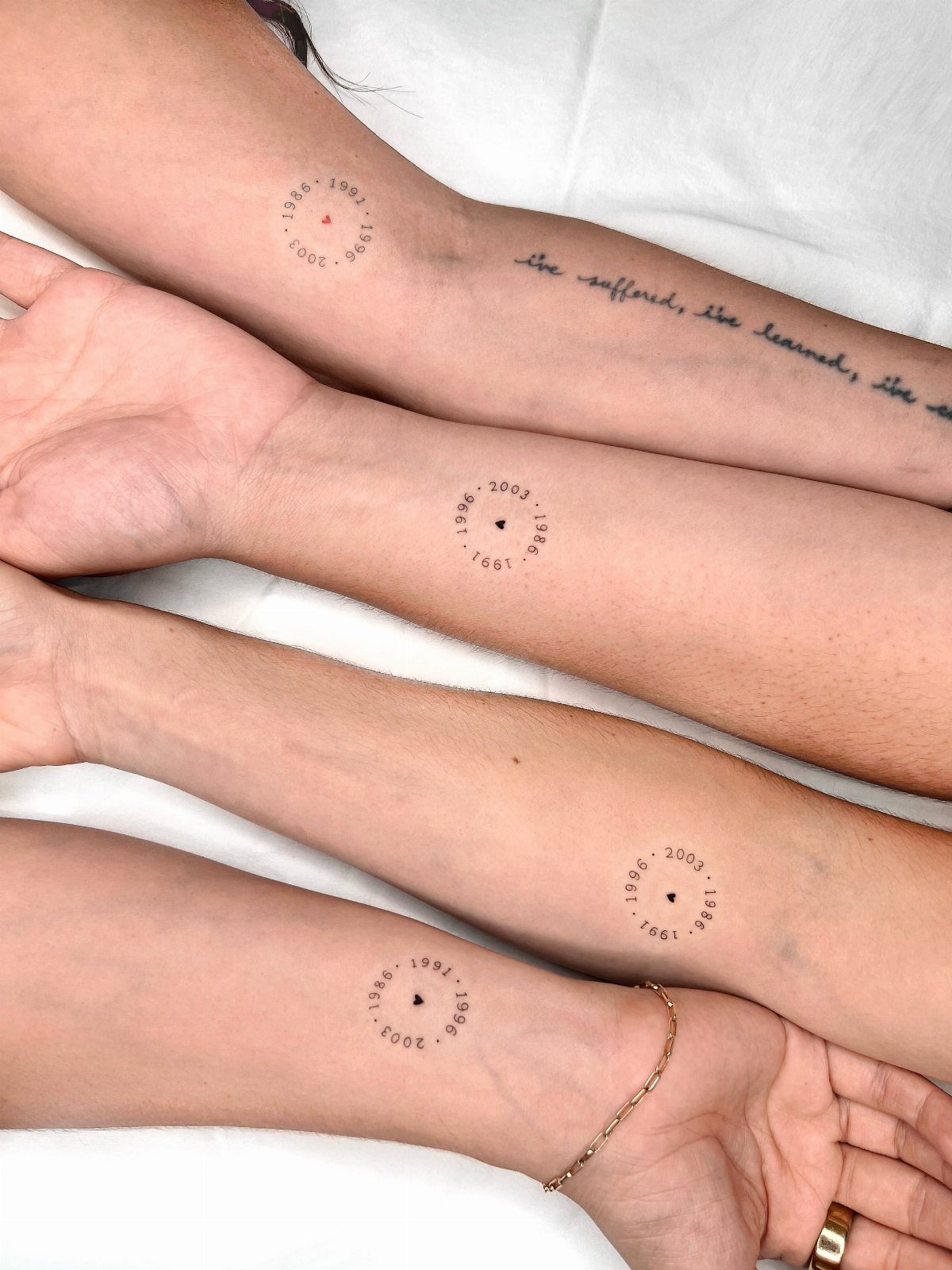 Four forearms with matching circular date tattoos on the inner wrists.