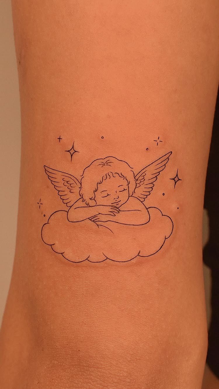Sleeping cherub angel tattoo resting on a cloud with small stars on skin.