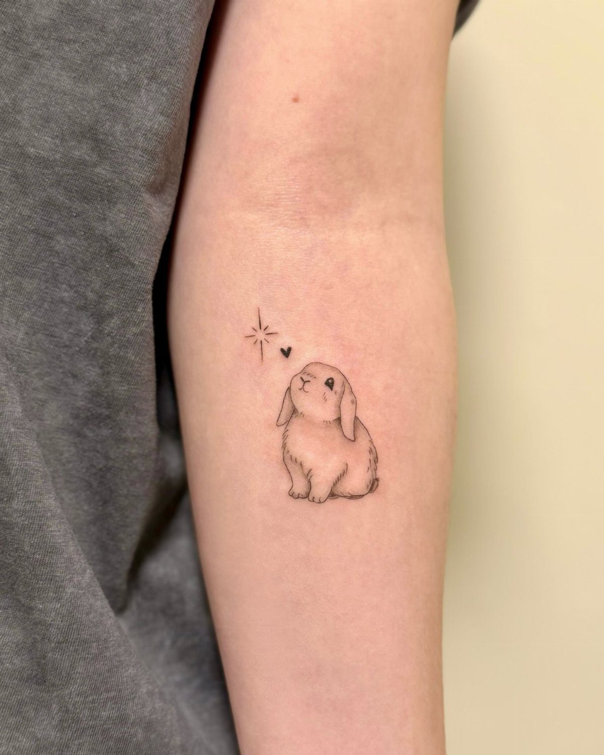 Small lop-eared rabbit tattoo with a tiny heart and star on a forearm.