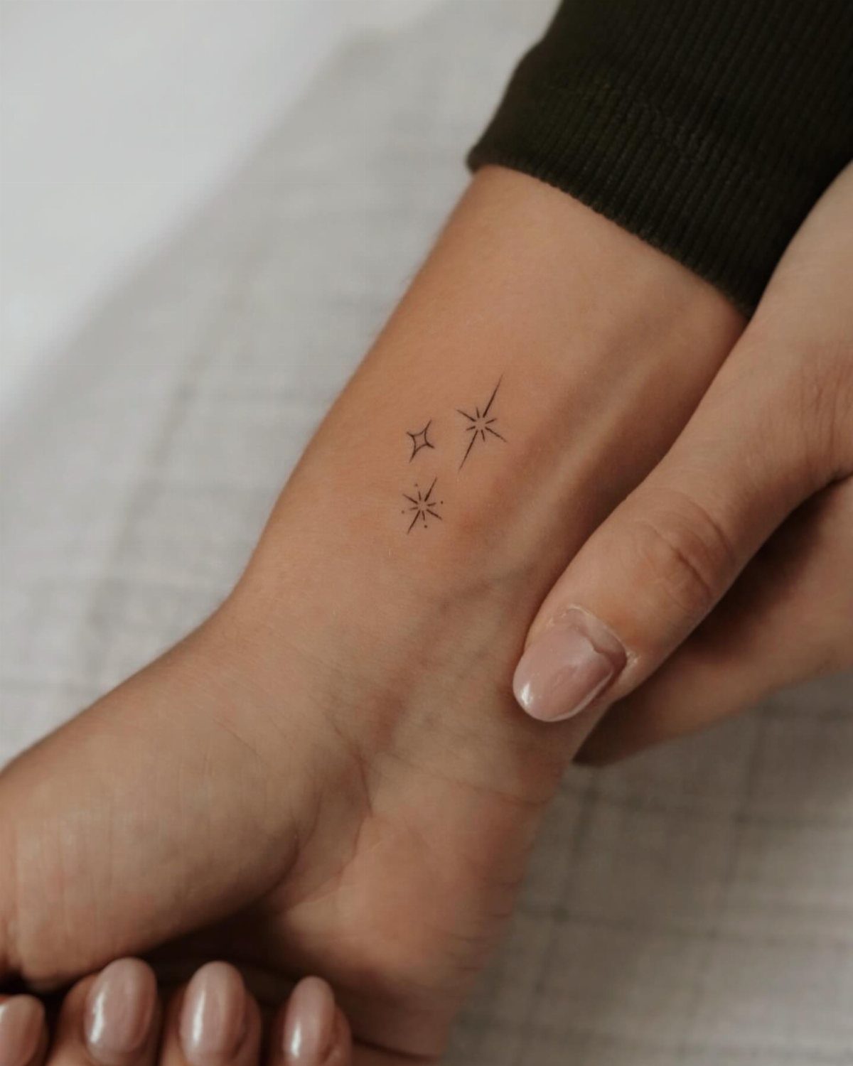 Three tiny black star tattoos on a person's inner wrist with neutral nails.