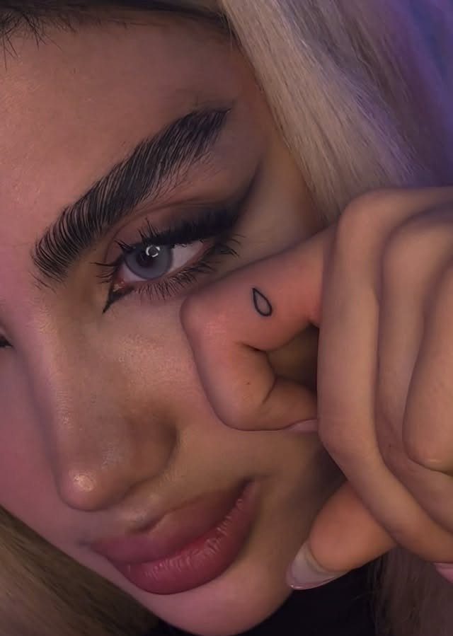 Woman with a small black teardrop tattoo on her finger near her face.