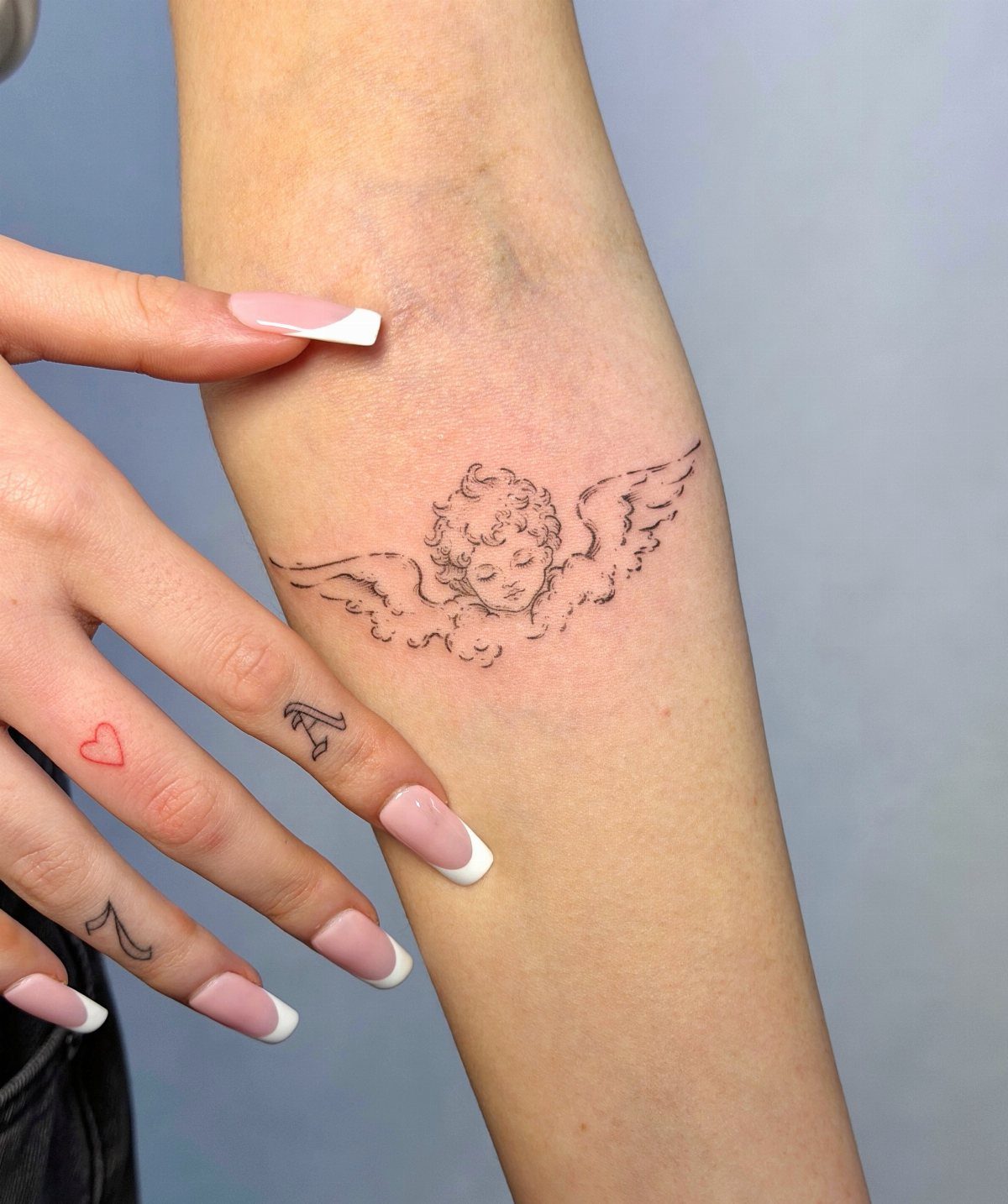 26 Small Pretty Tattoos for Butterflies, Stars, and More 15 Small fine-line cherub angel tattoo on a person's forearm with manicured nails.