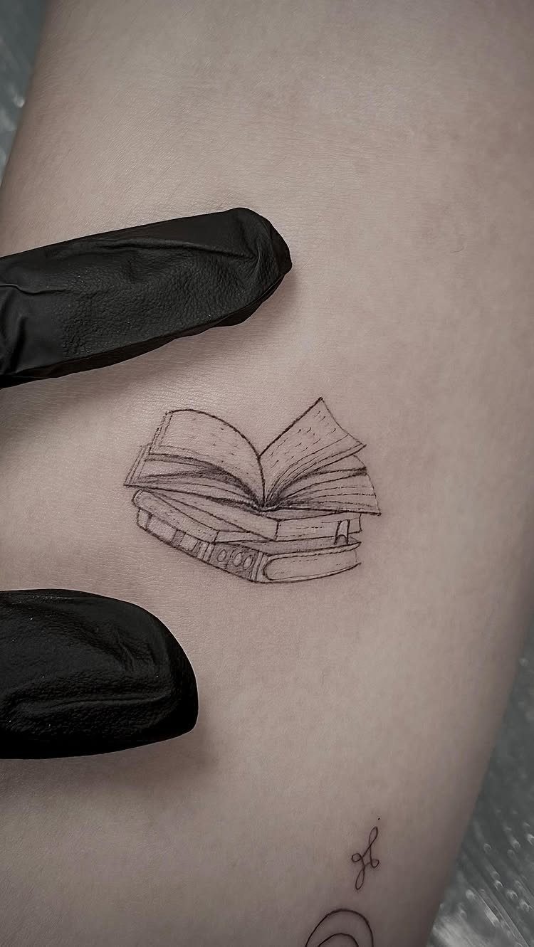 26 Small Pretty Tattoos for Butterflies, Stars, and More 21 Small black ink tattoo of an open book on a person's skin.