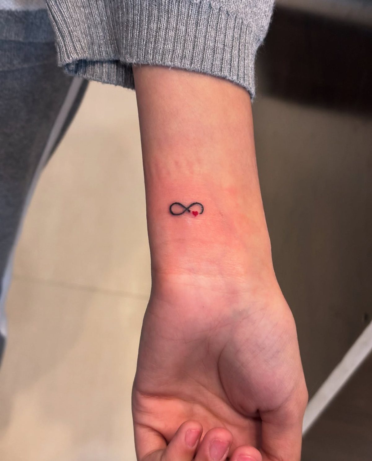26 Small Pretty Tattoos for Butterflies, Stars, and More 10 Small black infinity symbol tattoo with a red heart on a person's wrist
