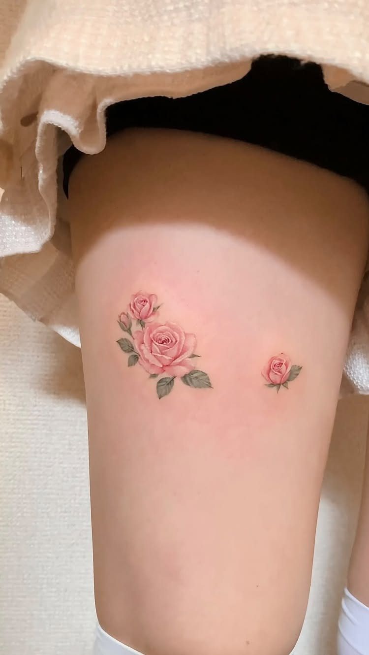 26 Small Pretty Tattoos for Butterflies, Stars, and More 6 Small pink rose tattoos with green leaves on a person's thigh.