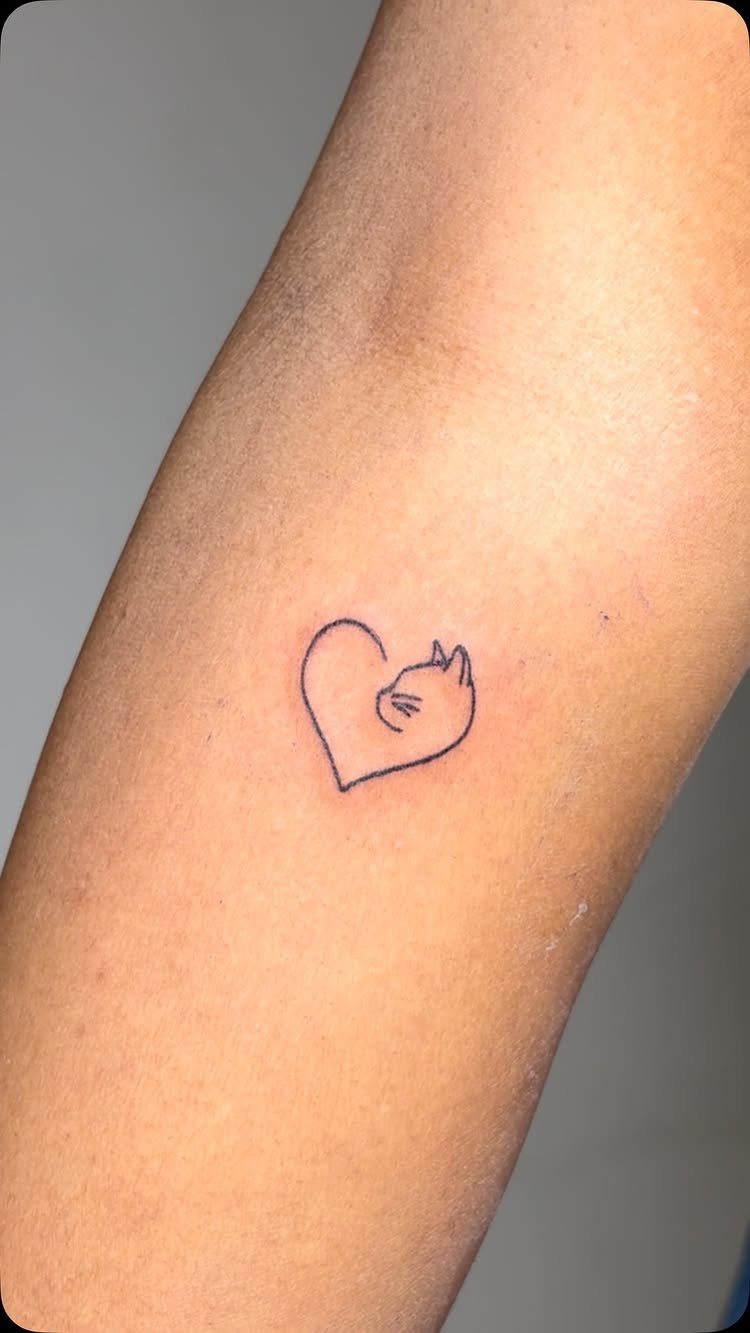 26 Small Pretty Tattoos for Butterflies, Stars, and More 4 Small black ink tattoo of a cat head shaped like a heart on skin