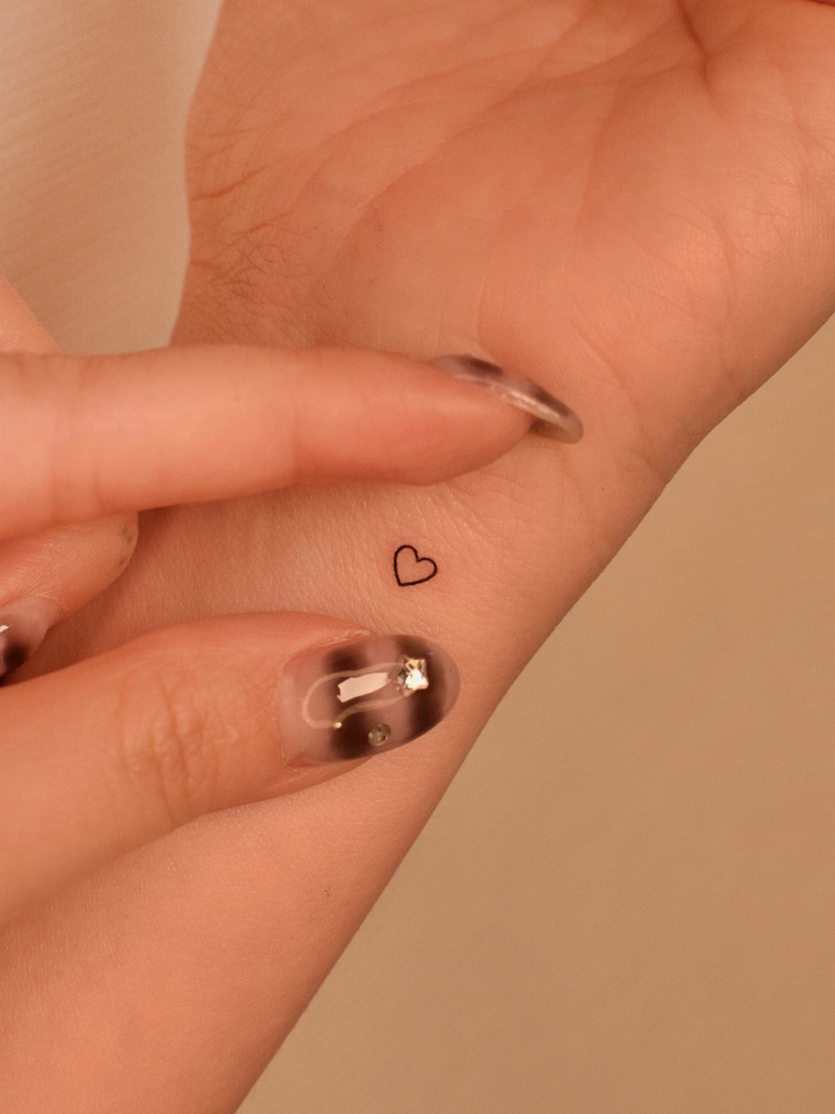 26 Small Pretty Tattoos for Butterflies, Stars, and More 3 Small black heart tattoo on a person's wrist with manicured nails pointing to it.