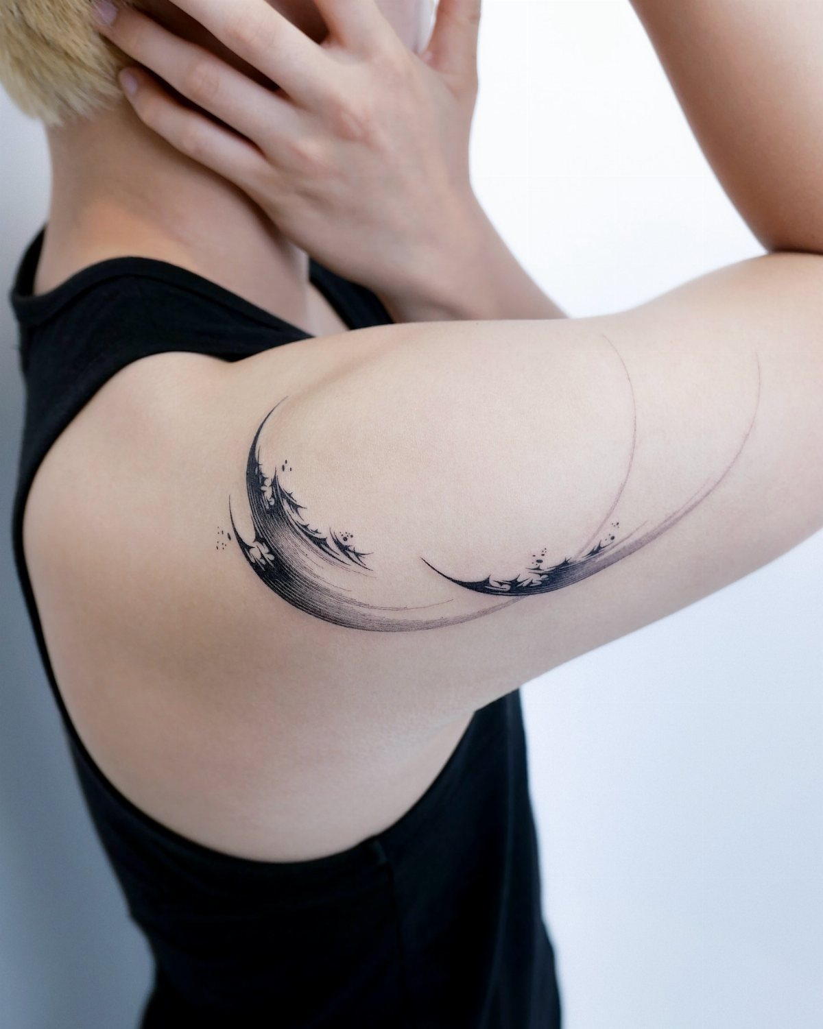 Black ink wave tattoo on a person's shoulder in a crescent shape