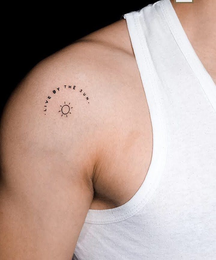 Small shoulder tattoo with a sun symbol and the quote Live By The Sun