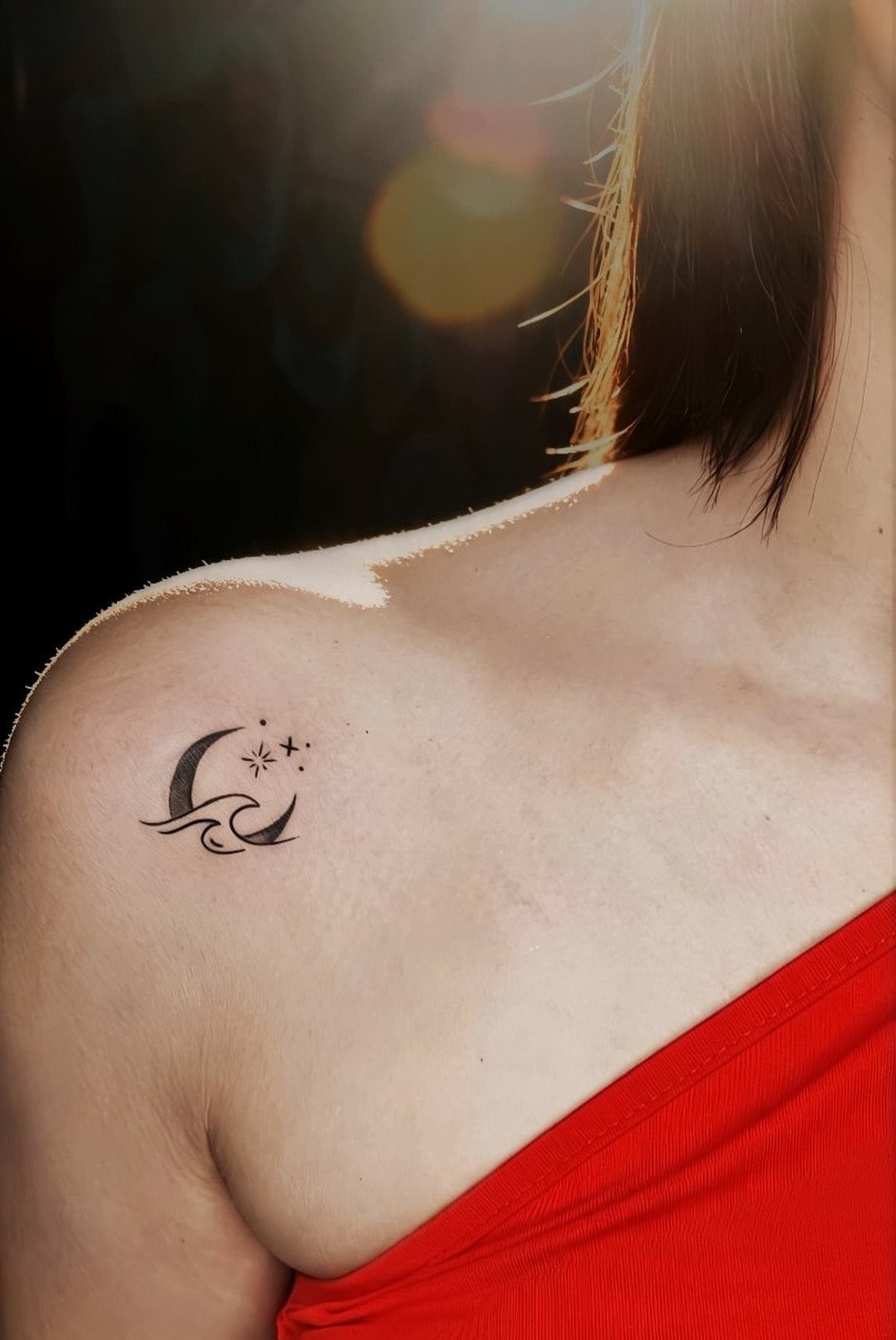 Crescent moon and star tattoo with a wave on a person's shoulder.