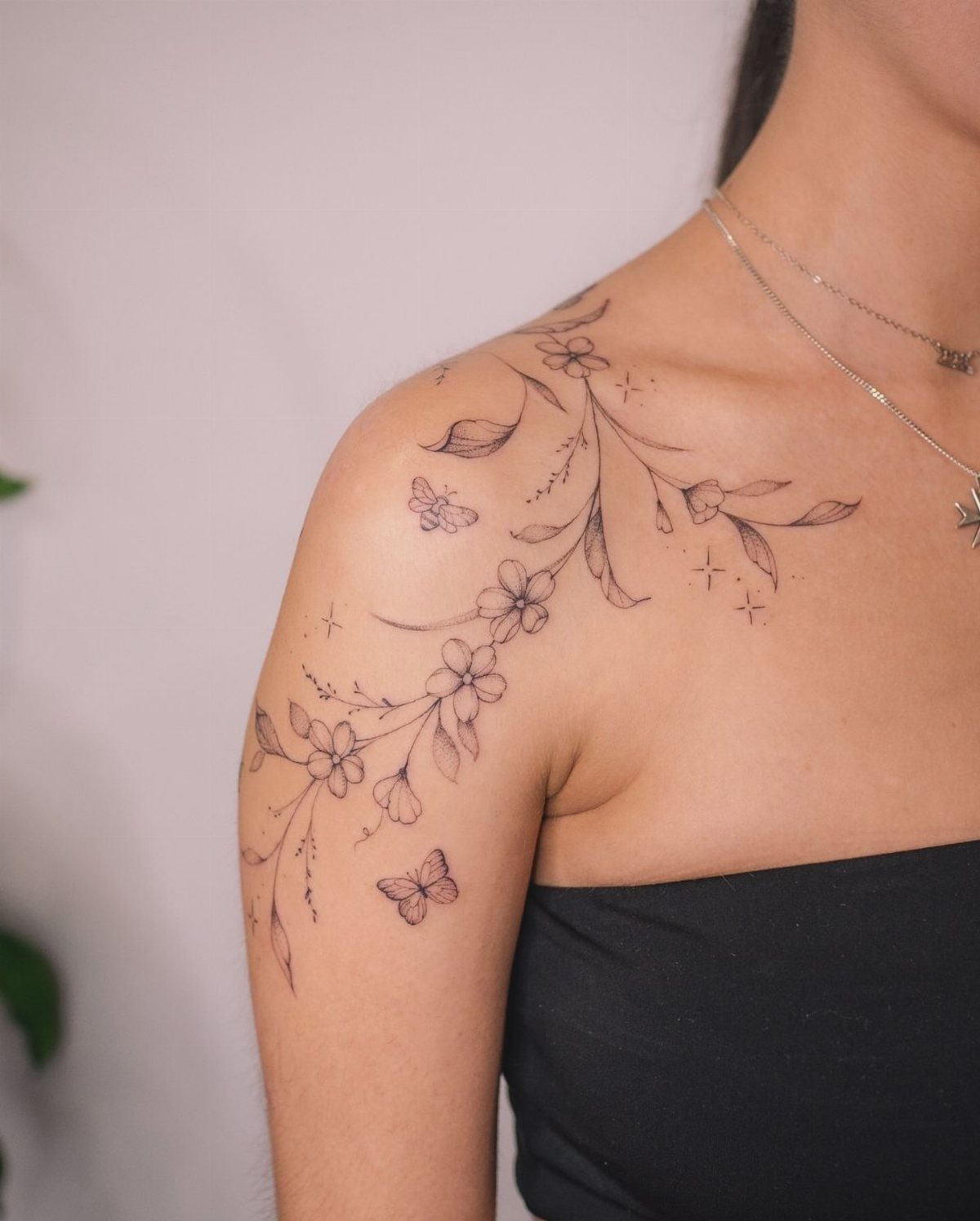 Fine-line tattoo of flowers, leaves, and butterflies on a person's shoulder and collarbone.