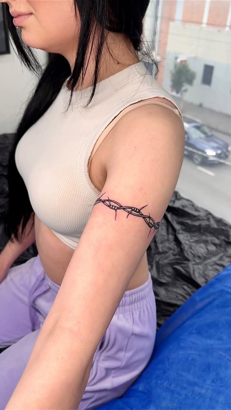 Barbed wire tattoo wrapping around a person's upper arm in black ink.