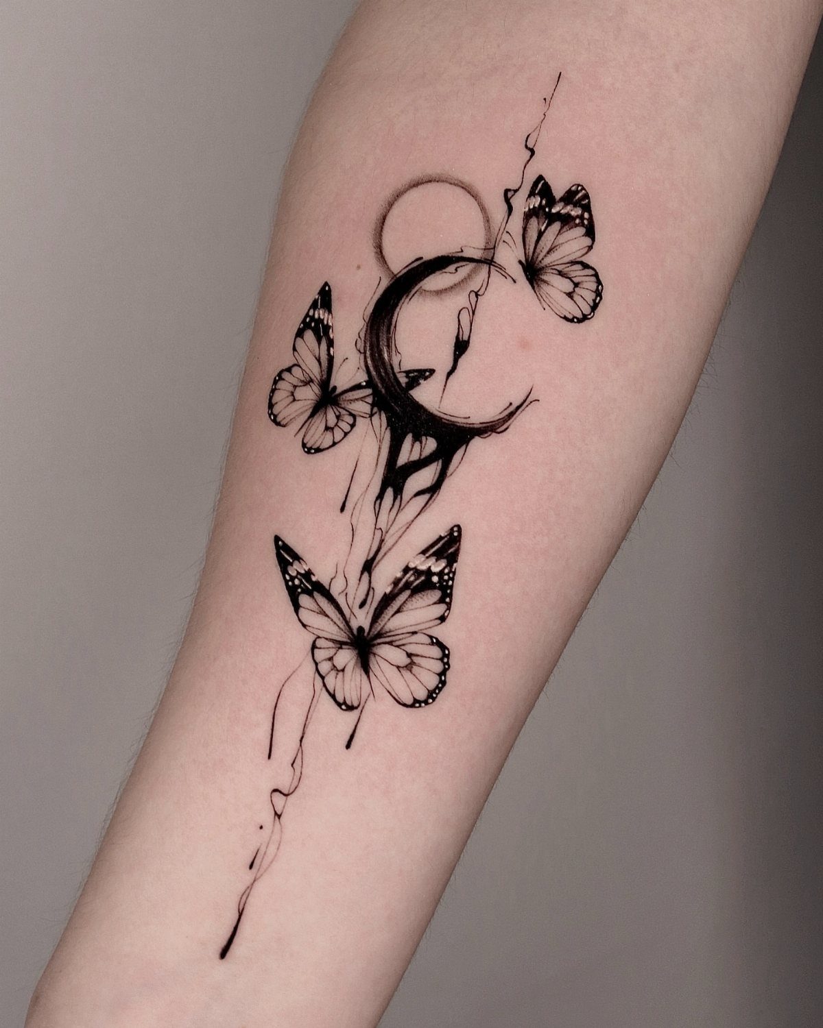 Crescent moon and butterfly tattoo with ink drips on a person's forearm