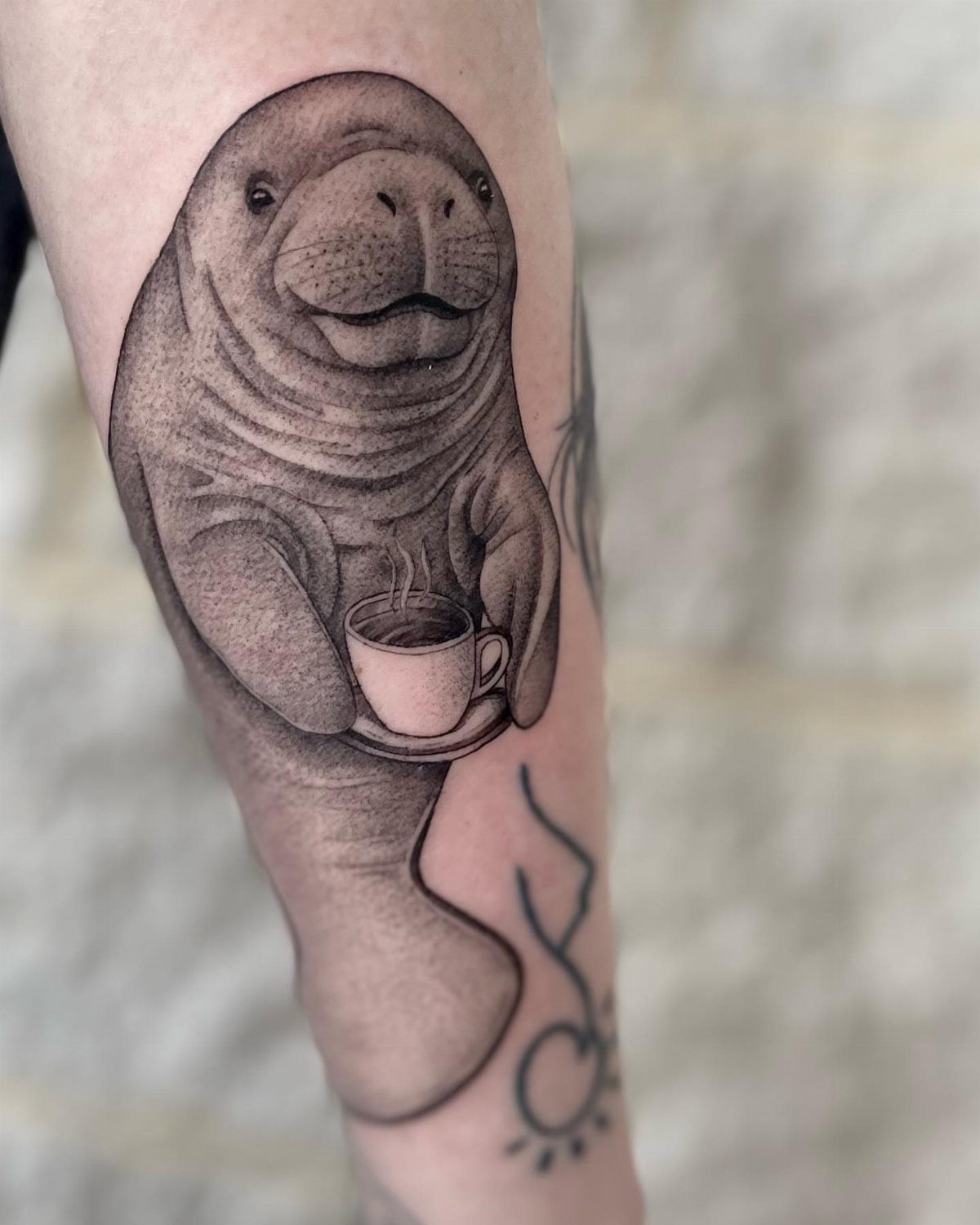 Manatee tattoo holding a coffee cup on a person's forearm