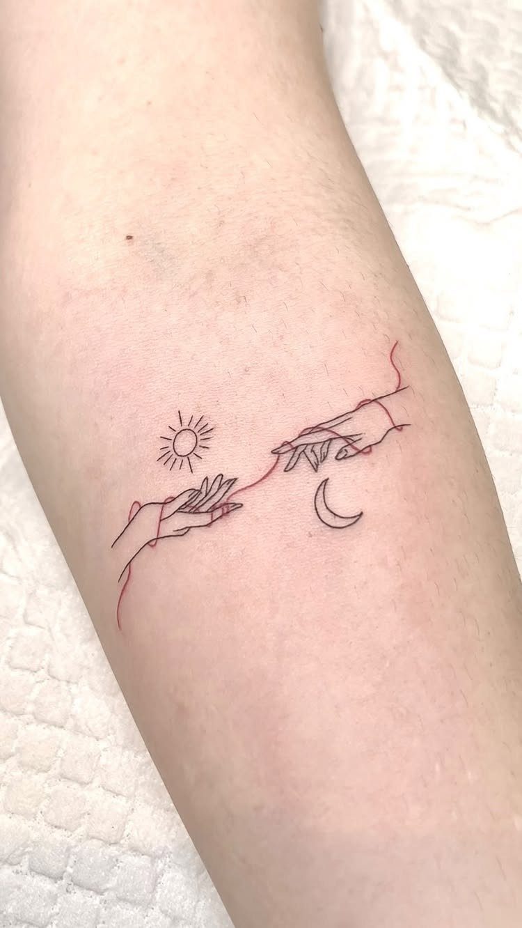 Two hands reaching toward each other with a sun and moon tattoo on forearm