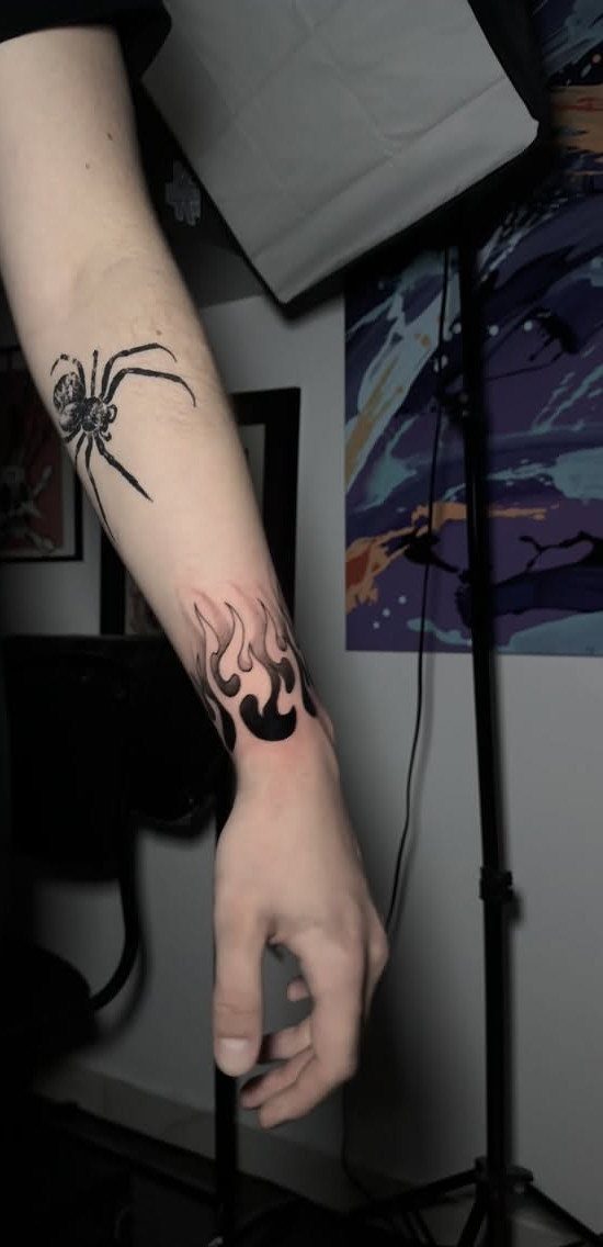 Flame tattoo wrapping around a wrist and a spider tattoo on the forearm.