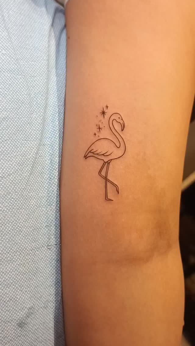 Small black ink flamingo tattoo with stars on a person's inner forearm.