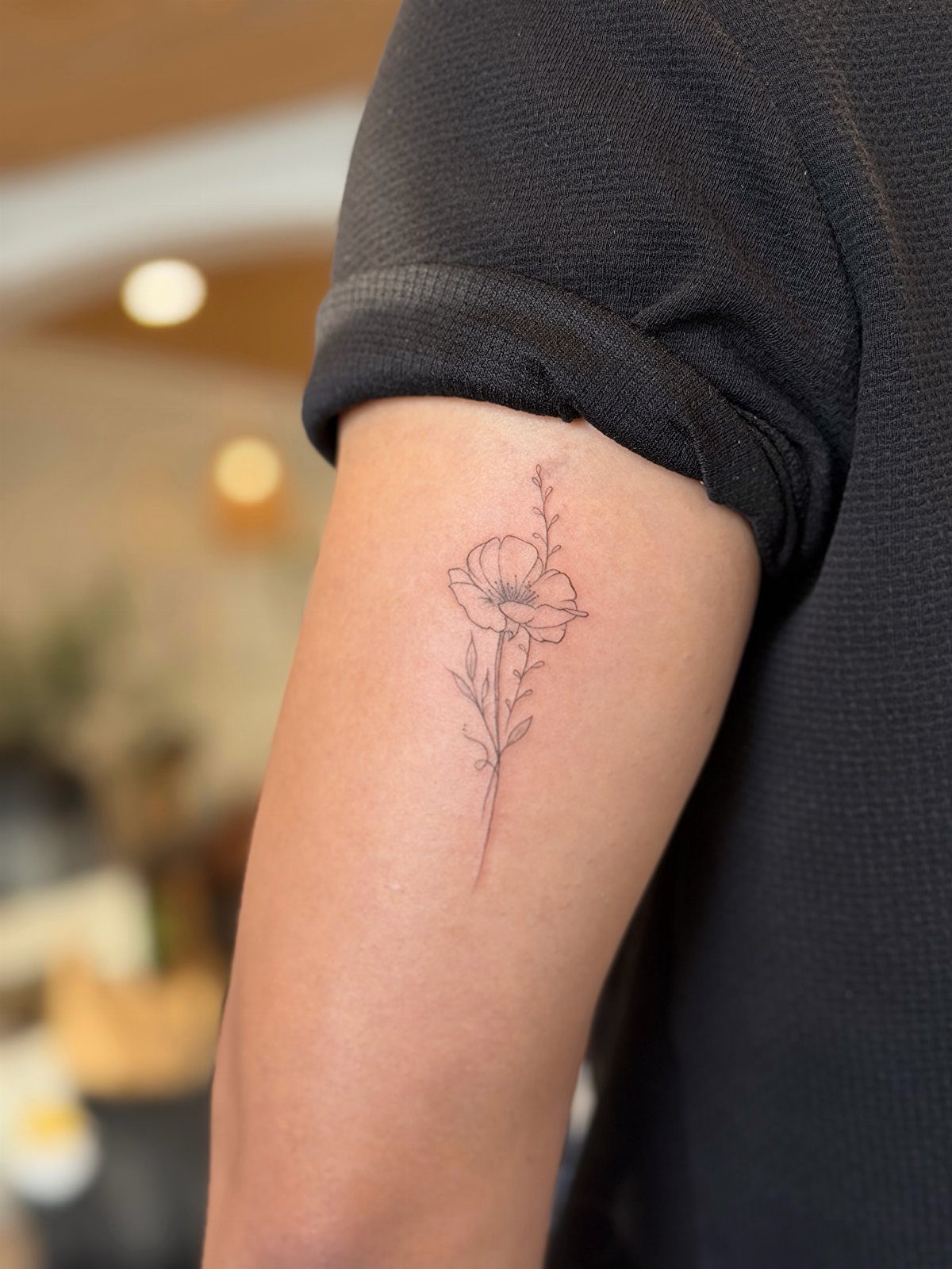 Small fine-line floral tattoo of a single flower on a person's upper arm
