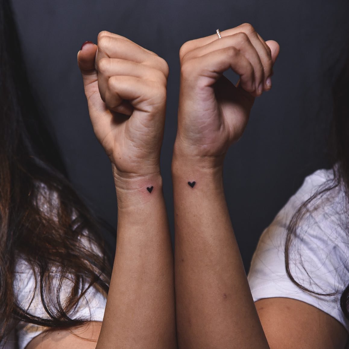 Two wrists side-by-side each featuring a small solid black heart tattoo.